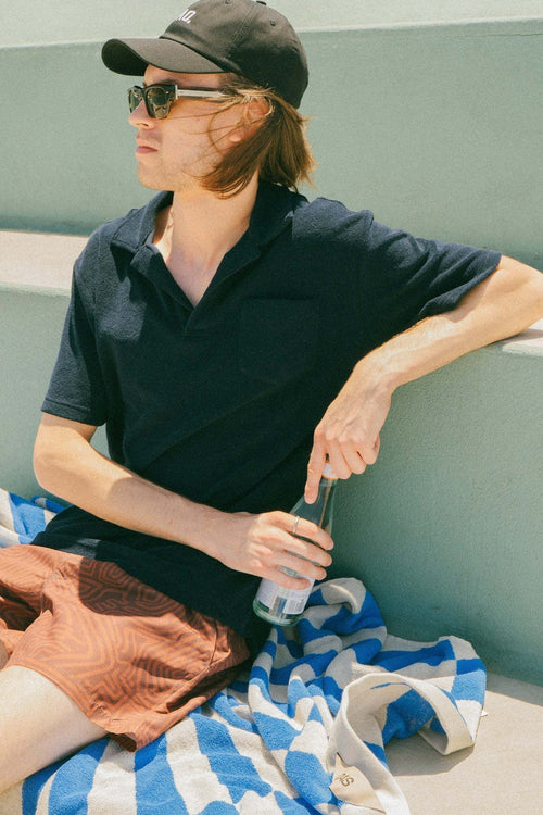 Man wearing OAS Navy Polo Terry Shirt in navy blue with palm tree embroidery, styled casually outdoors